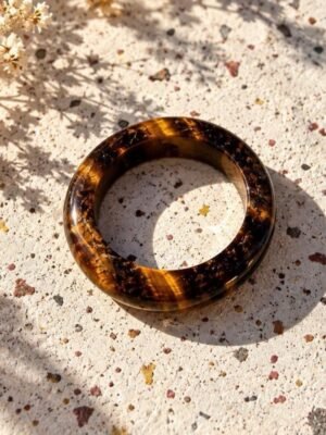 01-bague-mellia-oeil-de-tigre Bague MELLIA anneau en œil de tigre poli, reflets miel et brun, posée sur pierre beige avec fleurs séchées