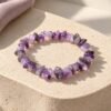 Bracelet élastique en éclats d'améthyste posé sur une pierre beige