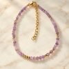01-bracelet-perles-lilas-amethyste Bracelet en fines perles d'améthyste lilas facettées et perles dorées posé sur du marbre