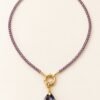 Collier en perles d'améthyste facettées avec anneau doré et pendentif goutte violet, posé à plat