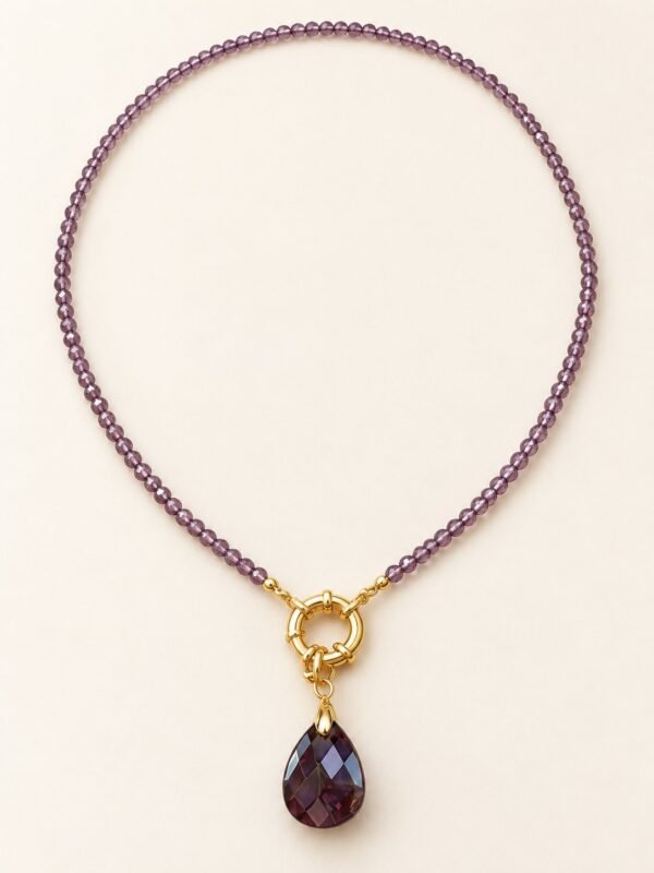 Collier en perles d'améthyste facettées avec anneau doré et pendentif goutte violet, posé à plat