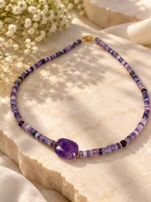 01-collier-perles-amethyste Collier en perles d'améthyste heishi lilas à violet, grande pierre centrale facettée et fermoir doré, posé sur pierre claire avec fleurs