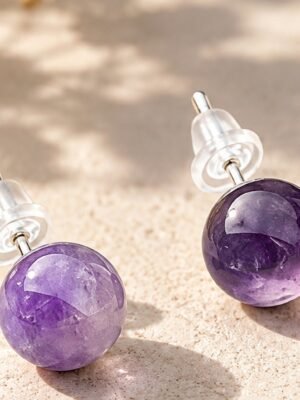 01-puces-oreilles-amethyste Puces d'oreilles en boules d'améthyste violette de 8 mm, tiges argentées et poussettes silicone, posées sur pierre beige