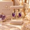 Boucles d'oreilles améthyste goutte sur présentoir, devant la boîte Serinaé