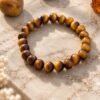Bracelet MELLIA en perles d’œil de tigre posé sur une dalle de marbre clair, à côté d’une pierre brute