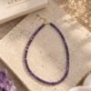 02-collier-perles-fines-amethyste Collier perles fines améthyste INTUITION posé sur dalle travertin, finition plaqué or, boîte Serinaé et améthyste brute