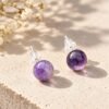 Paire de puces améthyste INTUITION, boules polies lilas à violet, sur dalle claire avec fleurs séchées