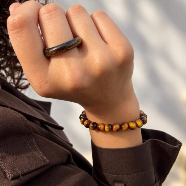 Bague MELLIA œil de tigre portée à l'index avec bracelet assorti, veste marron