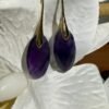 Boucles d'oreilles améthyste goutte posées sur un tissu blanc