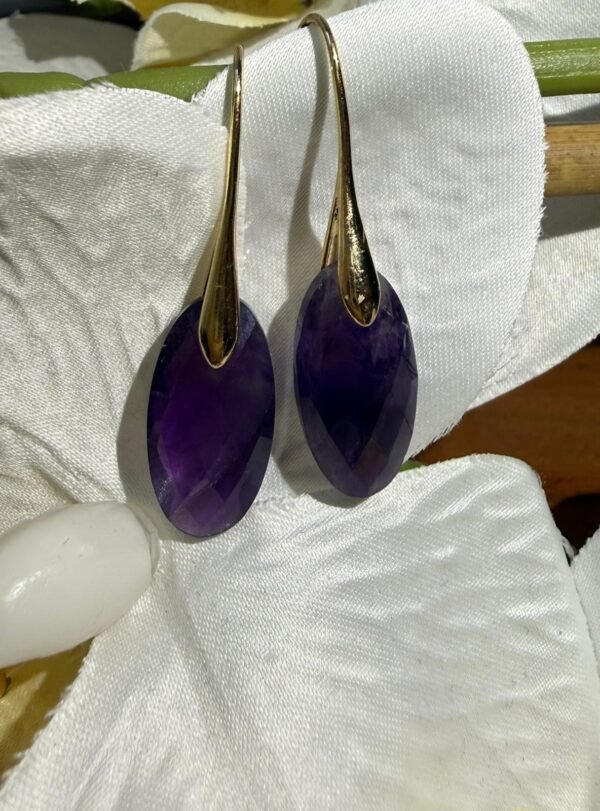 Boucles d'oreilles améthyste goutte posées sur un tissu blanc