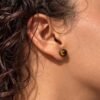 04-boucles-oreilles-mellia-oeil-de-tigre Puce d’oreille MELLIA en œil de tigre en gros plan sur le lobe, profil cheveux bouclés
