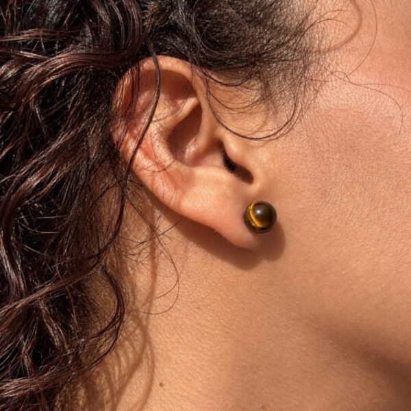 04-boucles-oreilles-mellia-oeil-de-tigre Puce d’oreille MELLIA en œil de tigre en gros plan sur le lobe, profil cheveux bouclés