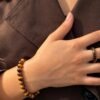 Bracelet MELLIA œil de tigre au poignet, main posée sur une chemise marron avec bague assortie