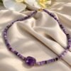 Collier Collection INTUITION en perles d'améthyste, pierre centrale facettée et détails dorés, posé sur satin avec orchidées