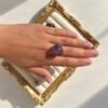 Main portant la bague roche améthyste Intuition en améthyste sur un cadre doré