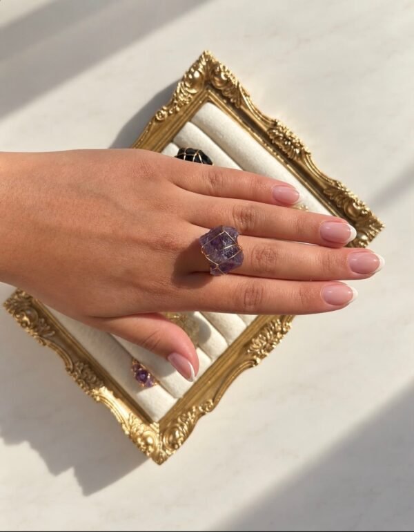 Main portant la bague roche améthyste Intuition en améthyste sur un cadre doré
