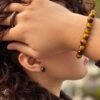 Bracelet MELLIA œil de tigre porté, main dans les cheveux, puce d’oreille et bague assorties