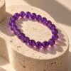 Bracelet perles d'améthyste 8 mm posé sur une pierre beige