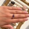 Main portant la bague mini Intuition en améthyste sur un cadre doré