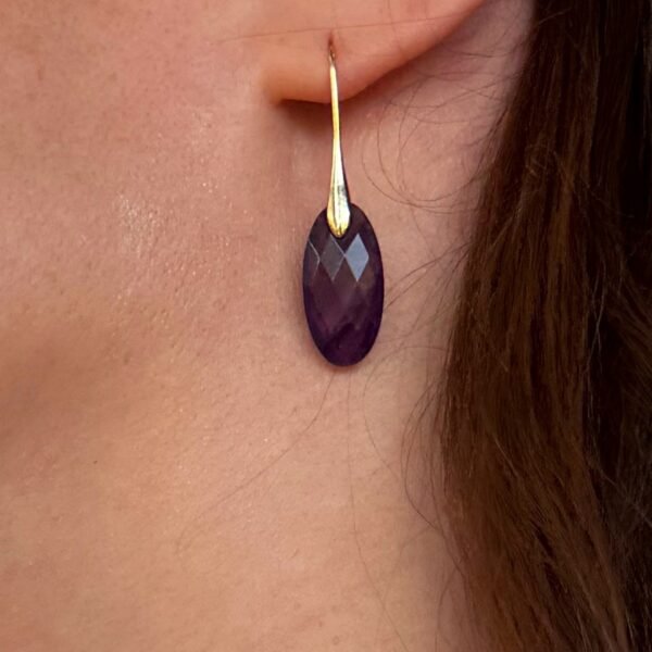 Gros plan sur une boucle d'oreille améthyste goutte portée à l'oreille