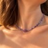 Collier en perles d'améthyste heishi porté au cou, lumière dorée, grande améthyste centrale et perles intercalaires dorées