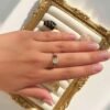Main portant la bague mini Intuition x Lina sur un cadre doré