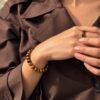 Bracelet MELLIA œil de tigre en gros plan sur le poignet, mains sur une chemise marron