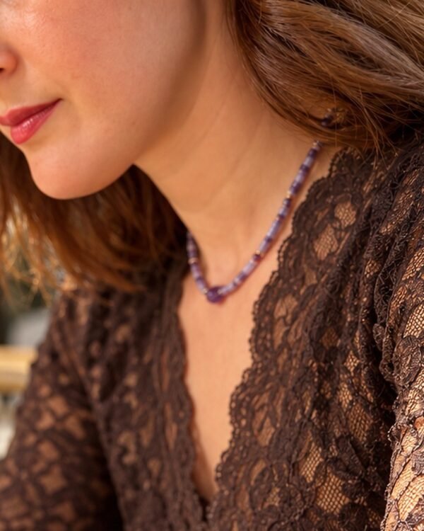 Collier perles améthyste porté de profil sur dentelle marron, bas du visage visible