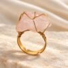 Bague brute en quartz rose naturel enlacée de fil, finition ton or, posée sur marbre – vue 1