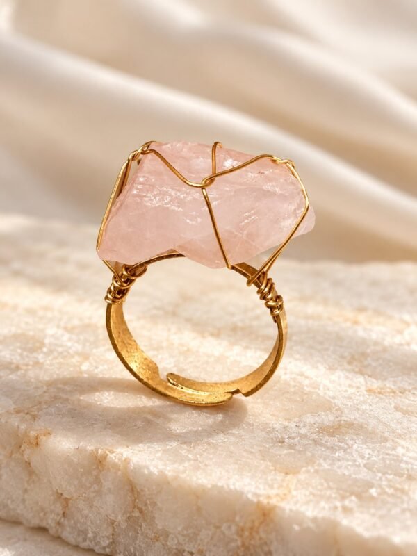 Bague brute en quartz rose naturel enlacée de fil, finition ton or, posée sur marbre – vue 1
