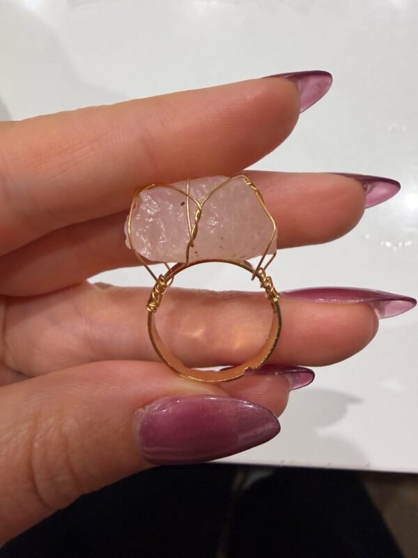 Bague brute en quartz rose naturel enlacée de fil, finition ton or, tenue entre les doigts – vue 3