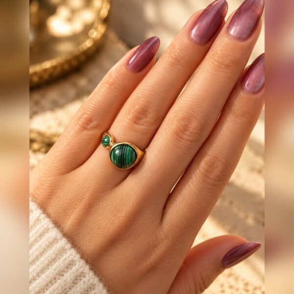 Bague MALYA en malachite portée au doigt, détail de la monture dorée