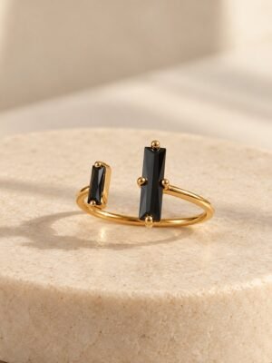 bague-nera-obsidienne-noire-1 Bague NÉRA ouverte, deux pierres rectangulaires en obsidienne noire sur anneau en cuivre couleur dorée, posée sur pierre claire – vue 1