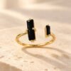 Bague NÉRA asymétrique en obsidienne noire et cuivre couleur dorée, de face sur pierre beige – vue 2