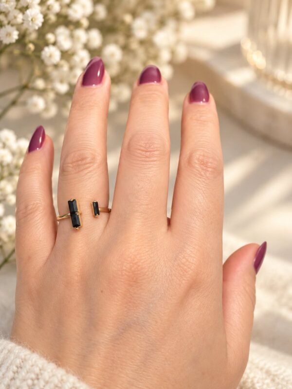 Bague NÉRA en obsidienne noire portée au doigt, fleurs de gypsophile en arrière-plan – vue 3