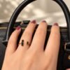Bague NÉRA en obsidienne noire portée, main posée sur un sac en cuir noir – vue 4