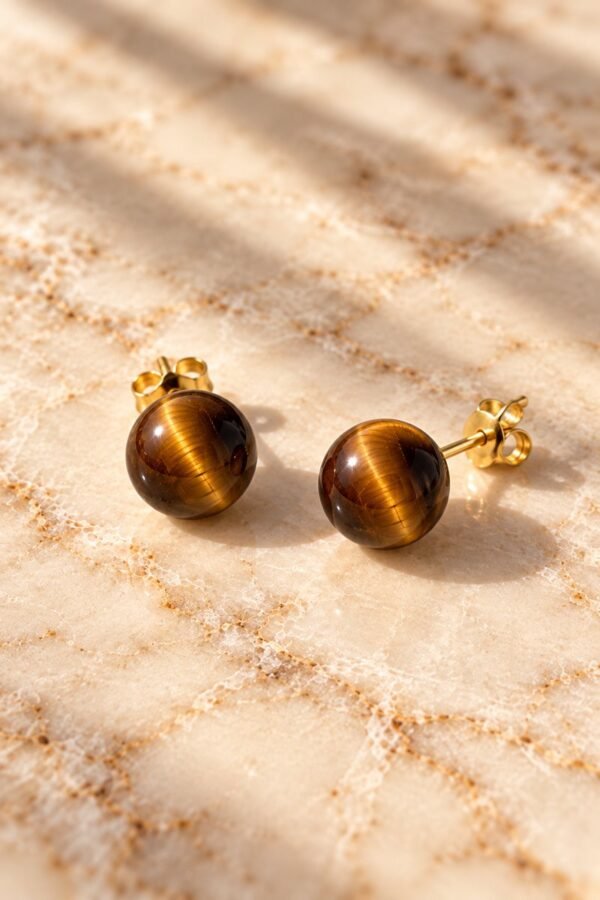 Boucles d’oreilles puces œil de tigre MELLIA Boucles d’oreilles puces MELLIA en œil de tigre naturel à bouchon, posées sur marbre clair – vue 1