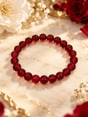 Bracelet GARANCE INTENSE en perles rondes de grenat naturel 8 mm, rouge rubis à bordeaux, posé sur marbre avec des roses – Serinaé