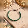 Bracelet MALACHITE 1 Bracelet ajustable en malachite, perles cylindriques vertes sur cordon marron, posé sur un bloc de pierre