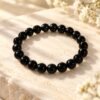 Bracelet NÉRA Noir Intense SERINAÉ en perles rondes d’obsidienne noire brillantes, posé sur une pierre claire