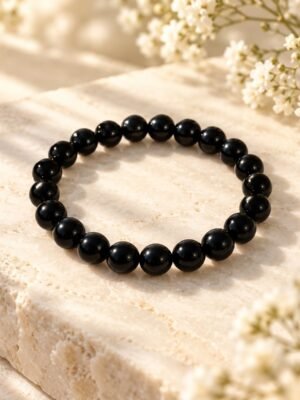 Bracelet NÉRA Noir Intense – perles d’obsidienne noire 1 Bracelet NÉRA Noir Intense SERINAÉ en perles rondes d’obsidienne noire brillantes, posé sur une pierre claire