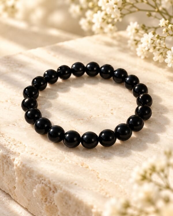 Bracelet NÉRA Noir Intense SERINAÉ en perles rondes d’obsidienne noire brillantes, posé sur une pierre claire