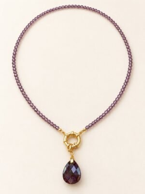 Collier AURA en perles d'améthyste facettées, anneau aux finitions dorées et pendentif goutte violet, posé à plat – Serinaé