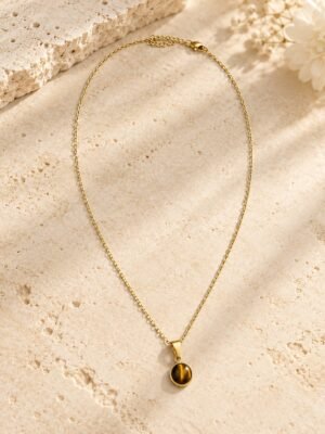 collier-medaillon-mellia-oeil-de-tigre-1 Collier médaillon MELLIA, cabochon rond en œil de tigre naturel sur fine chaîne plaquée or, posé sur pierre claire – vue 1