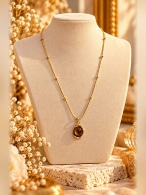 collier mellia goutte pendentif oeil de tigre buste Collier MELLIA GOUTTE, fine chaîne à billes aux finitions dorées et pendentif ovale aux nuances d'œil de tigre, sur buste crème – Serinaé