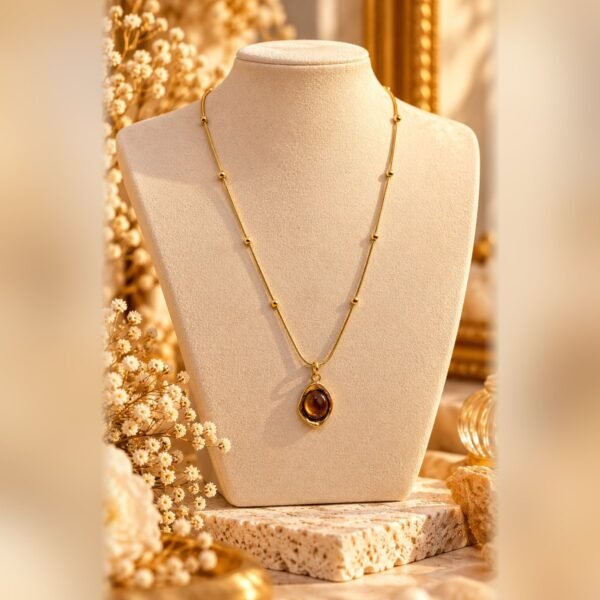 collier mellia goutte pendentif oeil de tigre buste Collier MELLIA GOUTTE, fine chaîne à billes aux finitions dorées et pendentif ovale aux nuances d'œil de tigre, sur buste crème – Serinaé