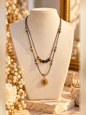 collier solea oeil de tigre soleil buste Collier SOLÉA double rang sur cordon marron, perles d'œil de tigre et pendentif soleil aux finitions dorées, porté sur buste crème – Serinaé