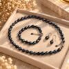 Parure ÉPURE Noire – perles d'eau douce noires 2 Parure ÉPURE Noire en perles d'eau douce noires aux reflets bleutés présentée dans un plateau